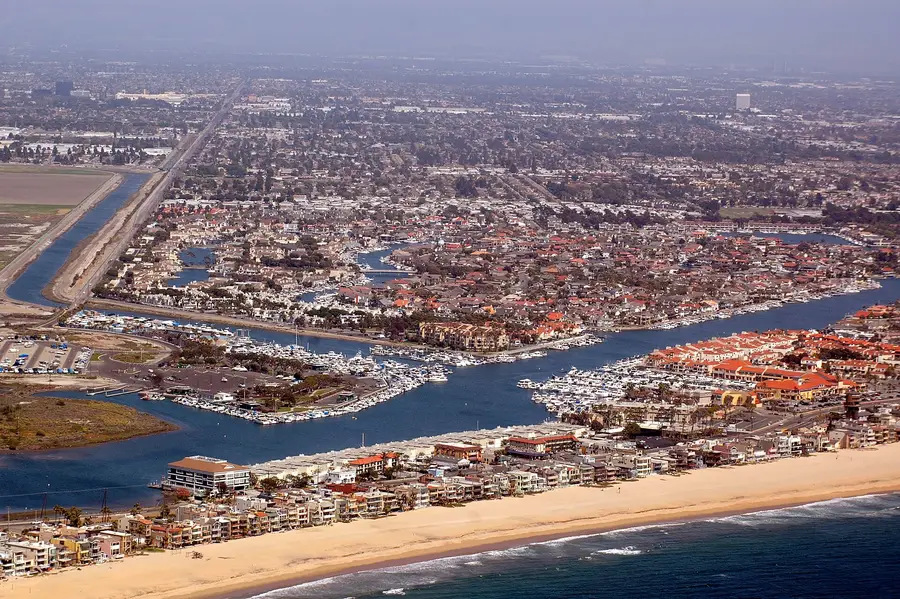 Aerial view of Huntington Harbour: marinas and boat slips along man-made channels, waterfront houses, and the beach and open ocean at the edge of the frame.